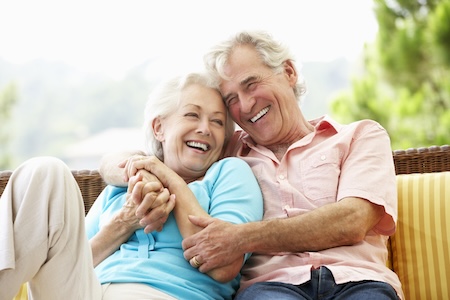 Senior Couple Sitting On Outdoor Seat Together Laughing